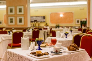 A dining area with tables set for breakfast, including croissants, pastries, and a fruit bowl. - Mariano IV Palace Hotel (Oristano)