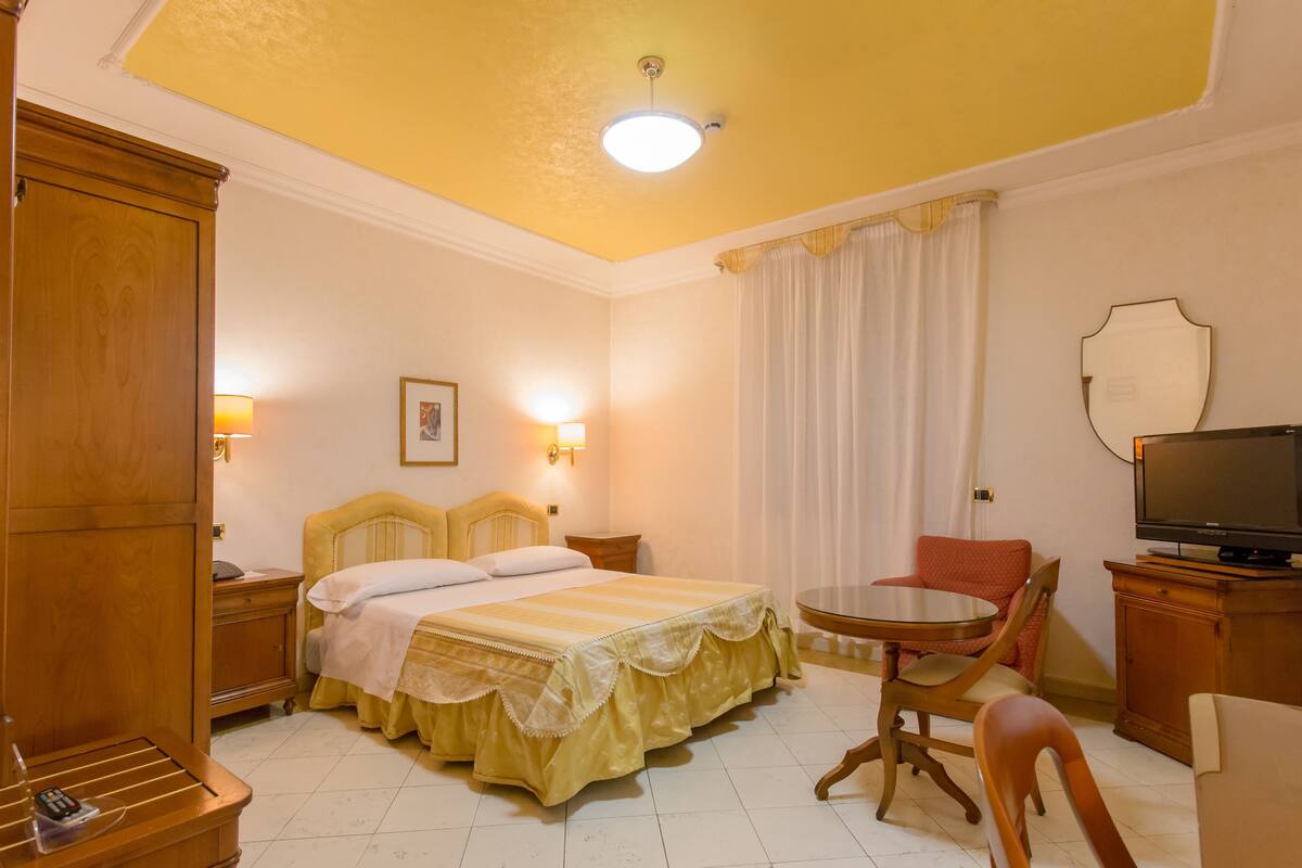Een hotelkamer met een bed, nachtkastjes, een televisie, een stoel en een klein tafeltje.