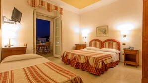 Habitación de hotel con dos camas, televisión, escritorio con lámpara y vista al exterior.