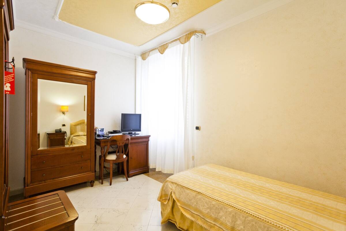 Een slaapkamer met een bed, een bureau met een computer, een stoel, een kledingkast en een spiegel.