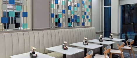 A modern restaurant with booths and tables, decorative glass panels, and a view of the city.