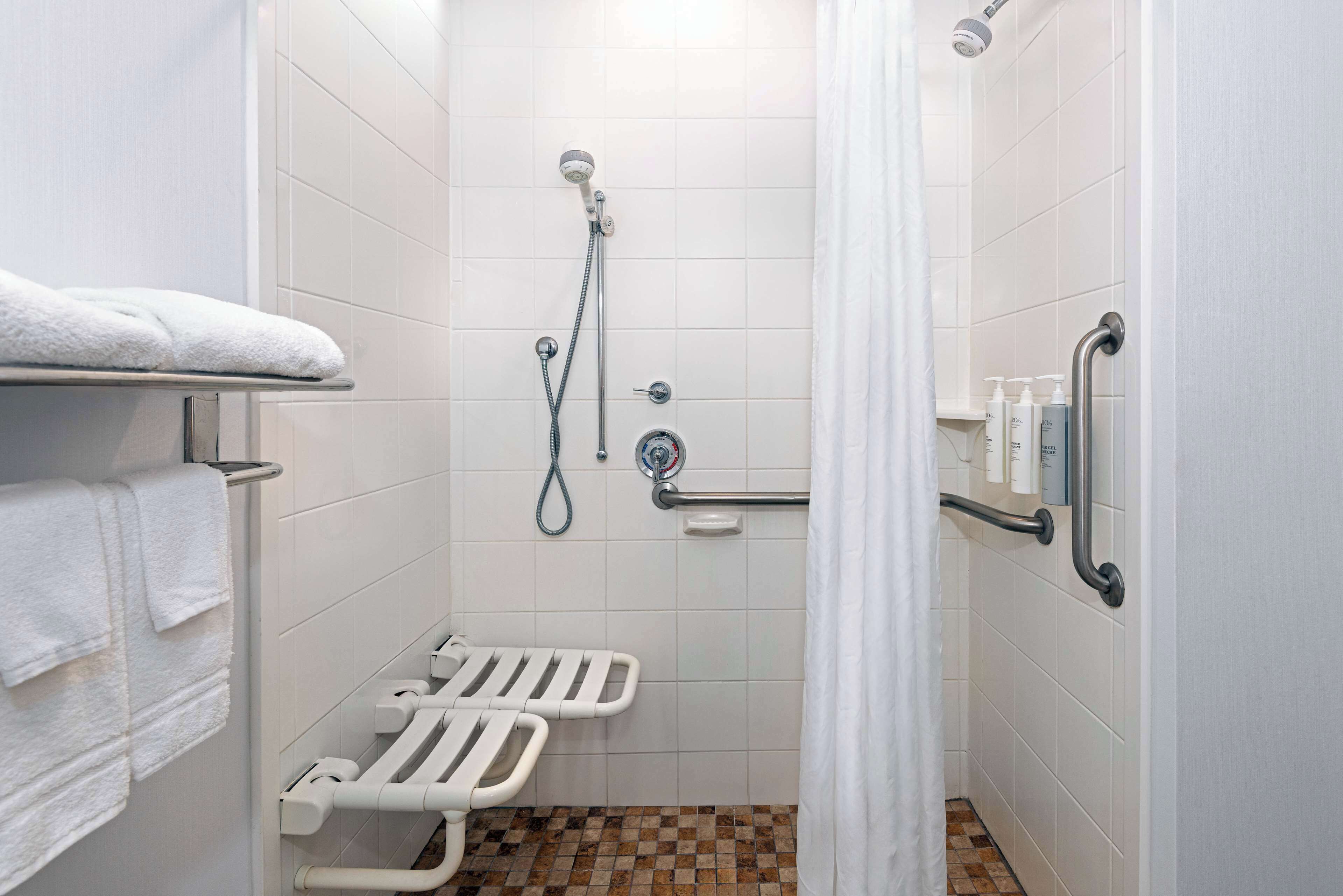Een badkamer met witte tegels, een douche met handdouche, een handgreep en een witte handdoekhouder.