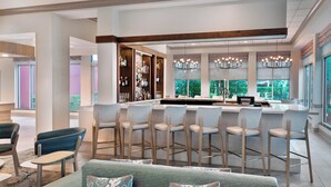 A modern bar area with multiple seating options, including bar stools and cushioned chairs, and a bar counter with a variety of bottles and glasses. - Hilton Garden Inn Tampa Airport Westshore (Tampa)