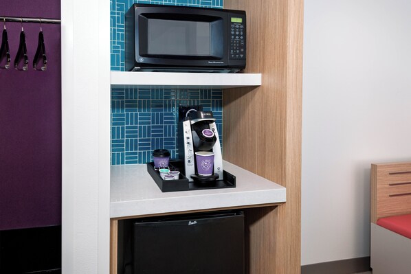 Una kitchenette compacta equipada con microondas, cafetera y refrigerador pequeño.