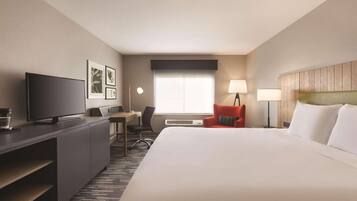 A hotel room with a large bed, a desk with a TV, a chair, and a window with blinds.