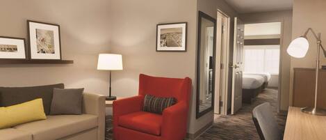 Una habitación de hotel con un sofá, un sillón rojo, una lámpara, un escritorio y una cama.