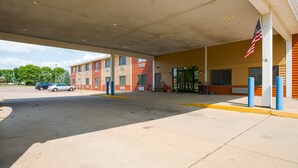 A building with a covered entrance, an American flag, and a parking lot with cars. - OYO Hotel Redwood Falls near Jackpot Casino (Redwood Falls)