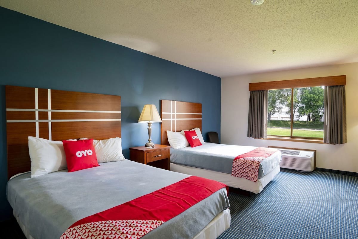 Une chambre d’hôtel avec deux lits, une table de chevet, une lampe, une fenêtre donnant sur un beau paysage et un luminaire au plafond.