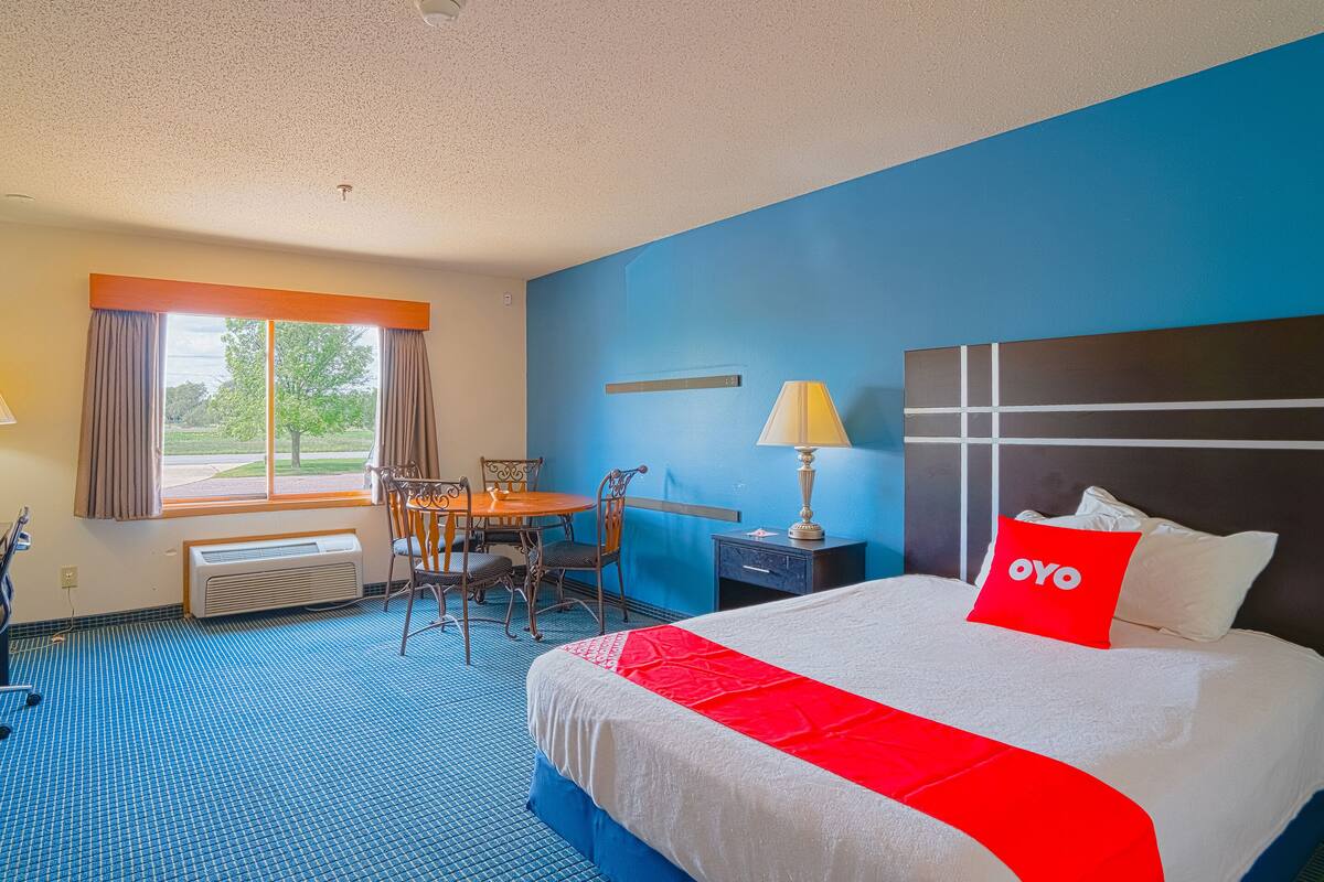 Une chambre d’hôtel avec un grand lit, un bureau, une chaise, une fenêtre avec des rideaux et une vue sur l’extérieur.
