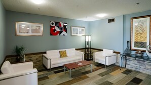 A living room with a white sofa, a coffee table, and a floor lamp. There are two framed pictures on the wall and a potted plant. - OYO Hotel Redwood Falls near Jackpot Casino (Redwood Falls)