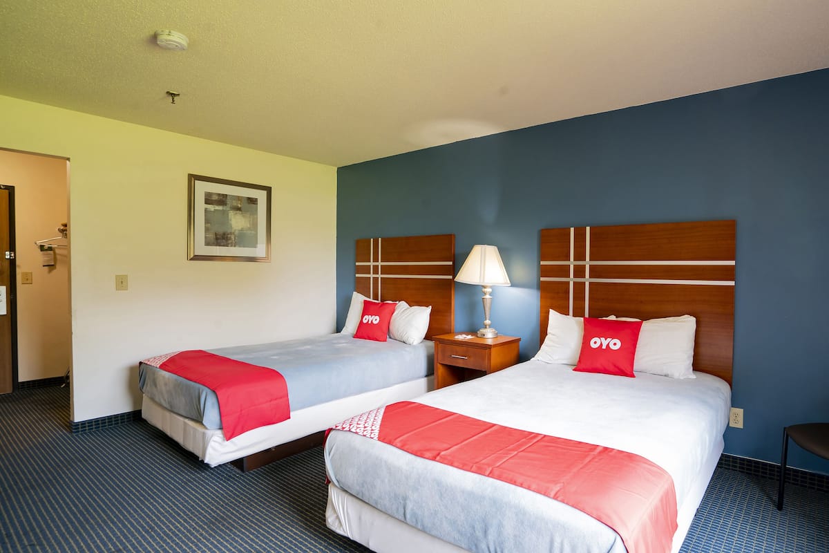 Une chambre d’hôtel avec deux lits, chacun recouvert d’une couverture rouge et blanche, dotée d’une tête de lit en bois et d’une table de chevet avec une lampe.