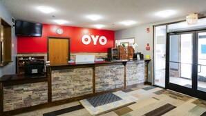 A reception area with a red wall, a wooden reception desk, a laptop, and a clock. - OYO Hotel Redwood Falls near Jackpot Casino (Redwood Falls)
