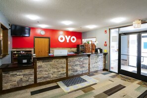 Una zona de recepción con pared roja, un mostrador de madera, una computadora portátil y un reloj.