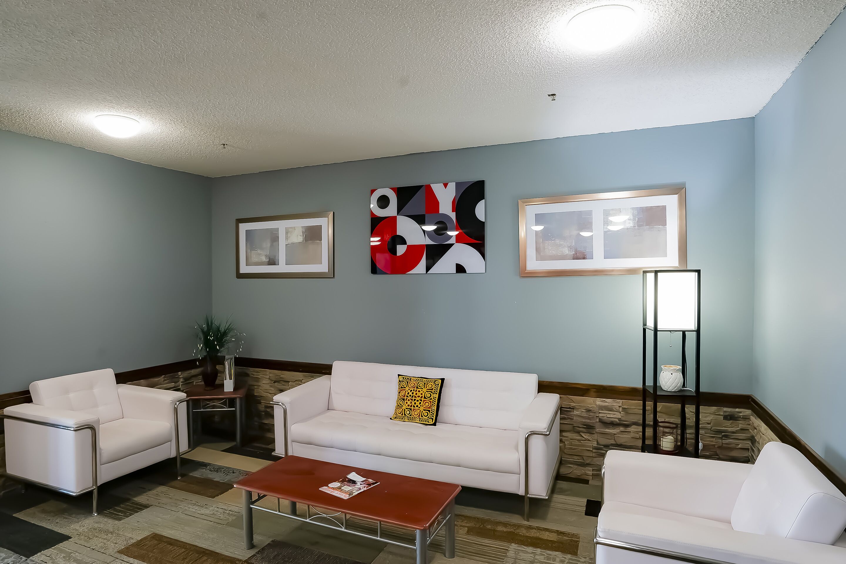 A modern living room with a white sofa, a coffee table, and a floor lamp. There are abstract paintings on the wall and framed pictures.