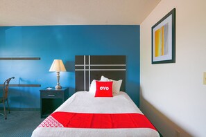 Habitación de hotel con cama, mesita de noche, lámpara, silla y un cuadro en la pared.