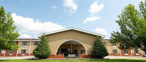 A building with a large arched entrance, a covered porch, and a lawn in front.