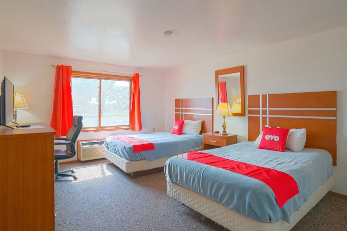 Une chambre d’hôtel avec deux lits, un bureau, une chaise, une fenêtre avec des rideaux et un miroir.