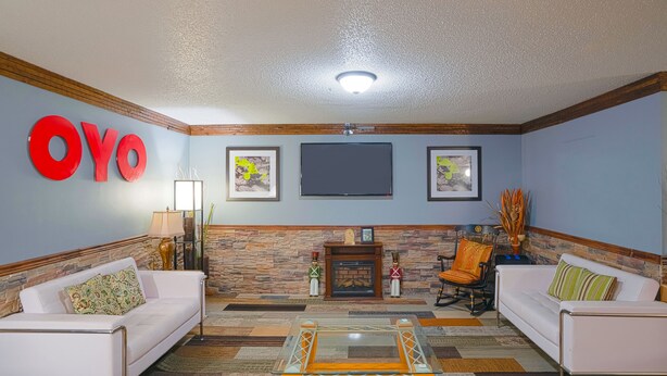 A living room with two white sofas, a glass coffee table, a fireplace, and a mounted TV. - OYO Hotel Redwood Falls near Jackpot Casino (Redwood Falls)