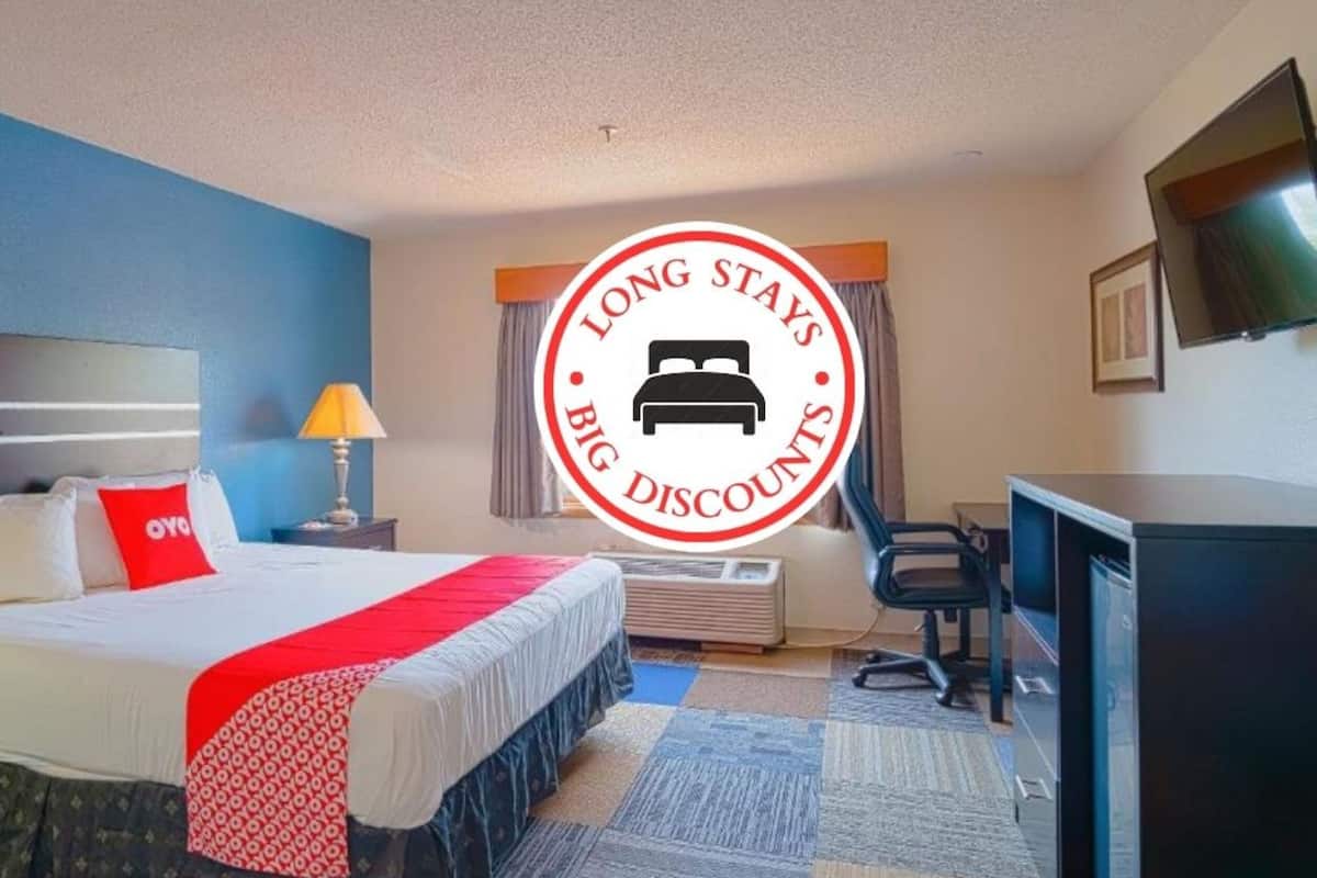 Une chambre d’hôtel avec un lit, un bureau, une chaise, une télévision et une fenêtre avec des rideaux.