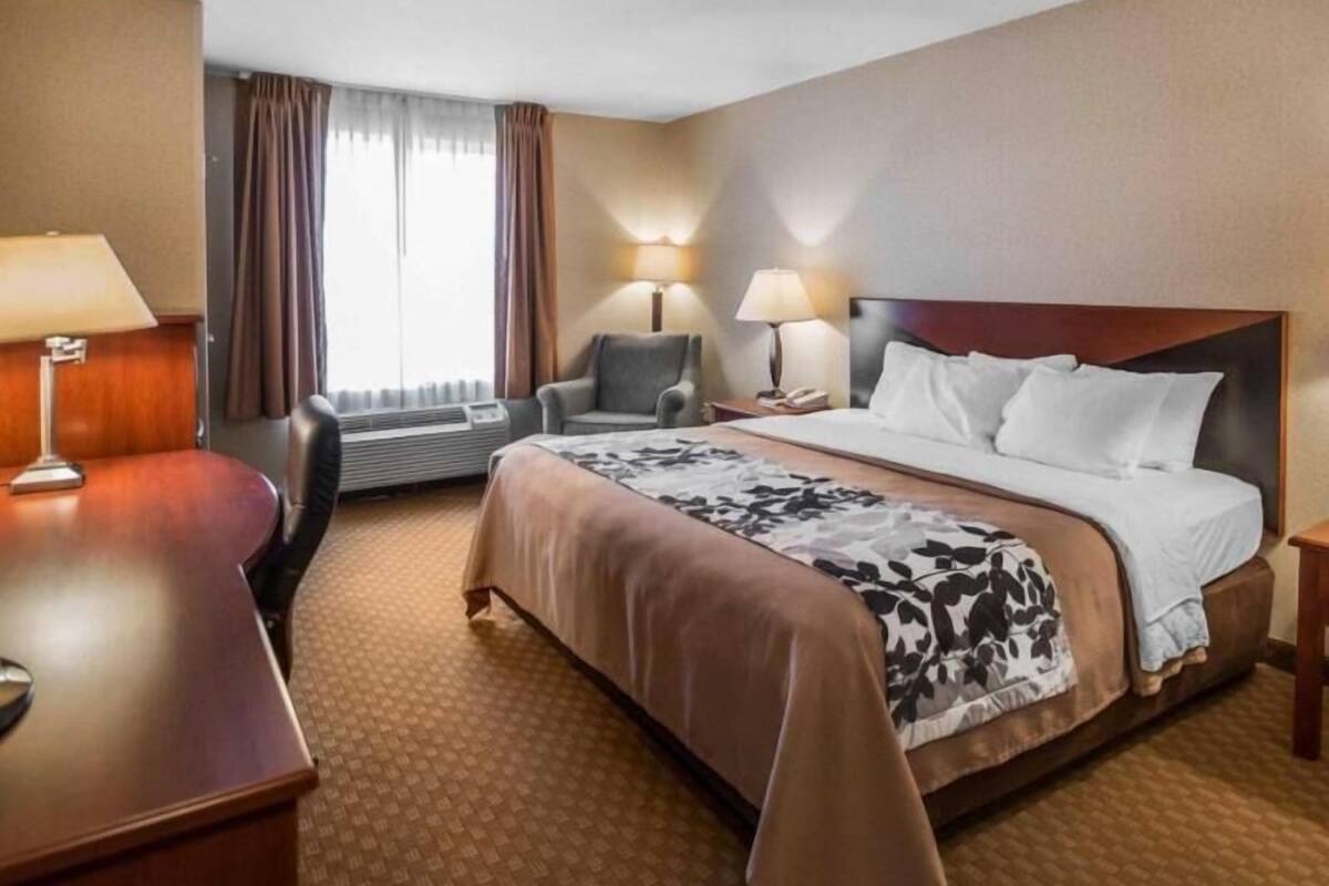 A hotel room with a bed, two chairs, a desk, a lamp, and a window with curtains.