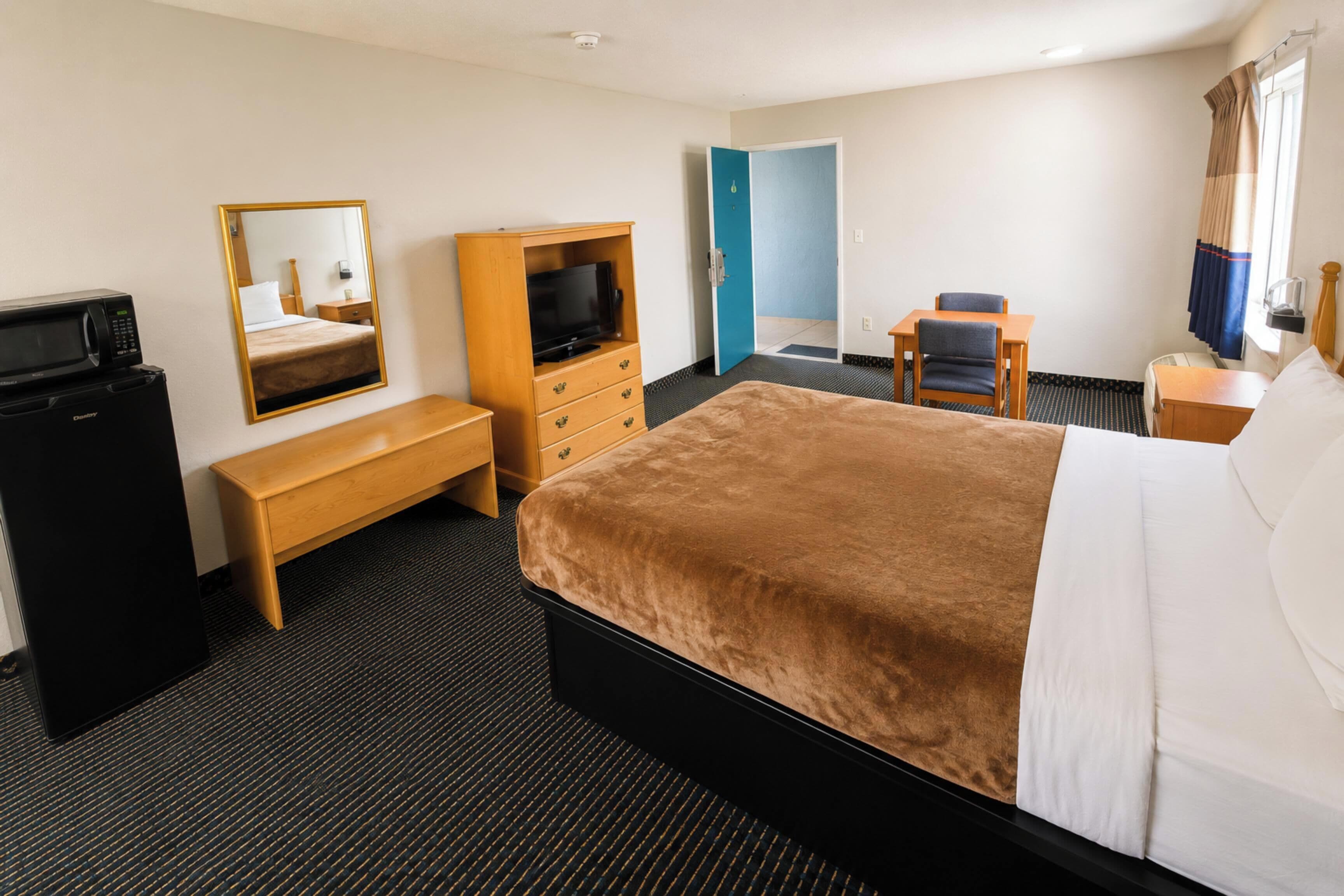 A hotel room with a bed, a TV, a desk, a chair, a mirror, and a wardrobe.