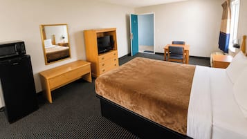 A hotel room with a bed, a TV, a desk, a chair, a mirror, and a wardrobe.