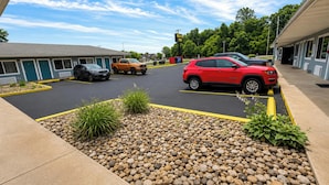 A parking lot with several SUVs, a building with a sign reading 'RELAX Inn,' and a landscaped area with rocks and plants. - Relax Inn Dover Near Speedway (Dover)
