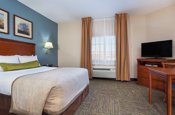 Quarto de hotel com cama, escrivaninha, televisão e janela com cortinas.