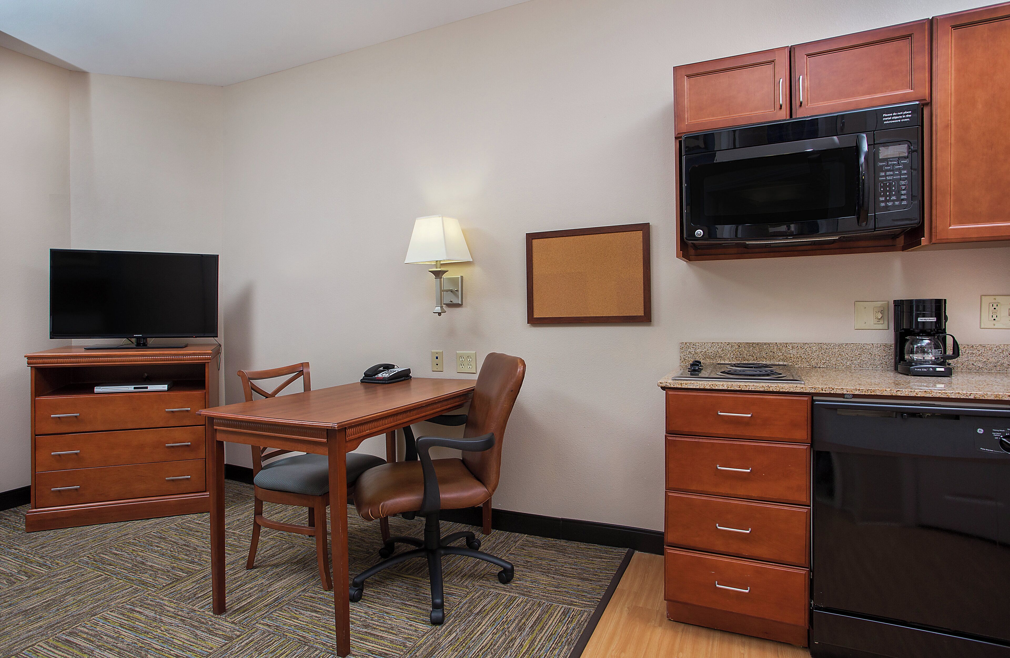 A hotel room with a dining table, a TV, a microwave, a coffee maker, and a desk with drawers.