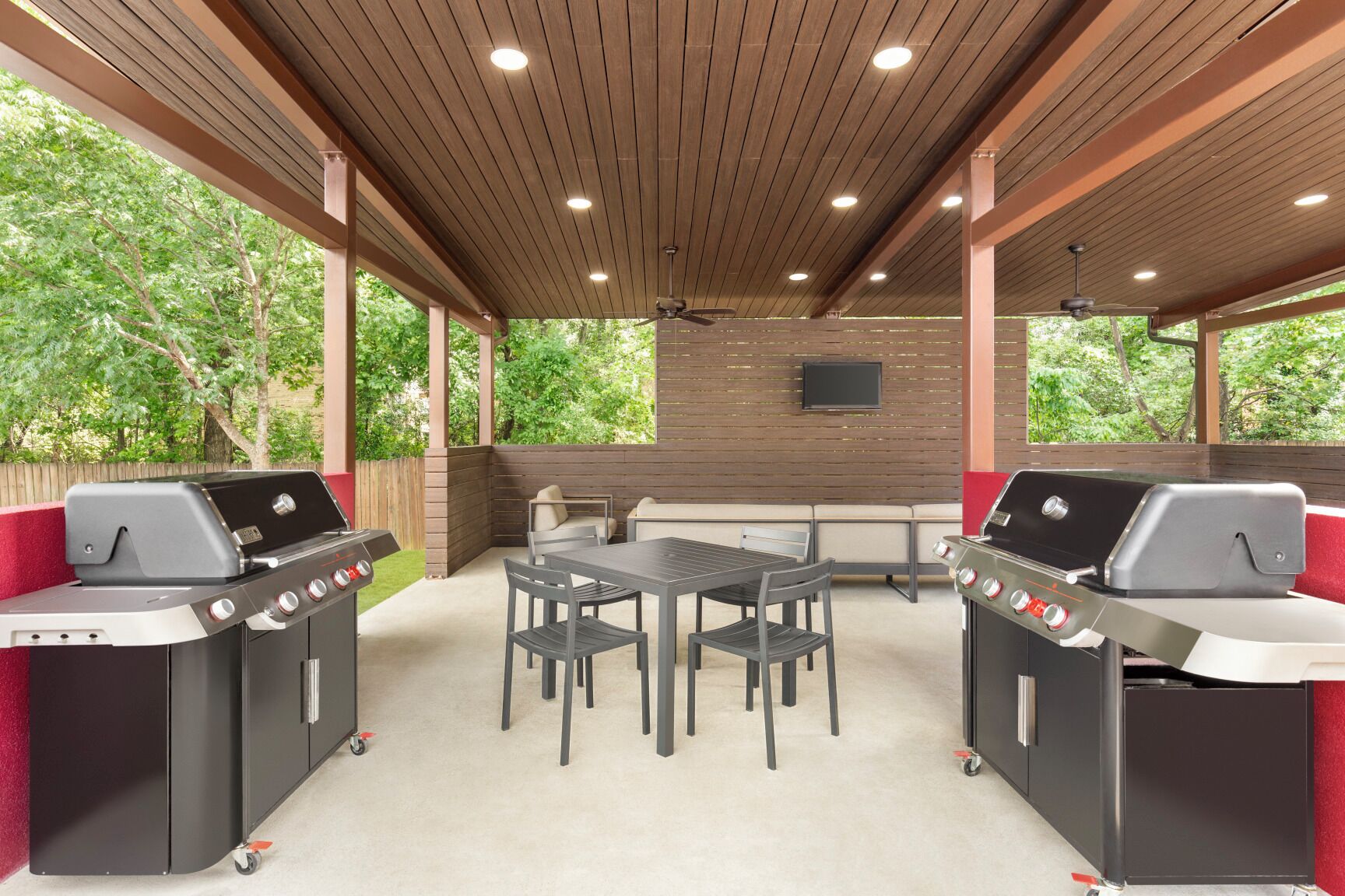 An outdoor patio with two barbecue grills, a table with chairs, and a TV mounted on the wall.