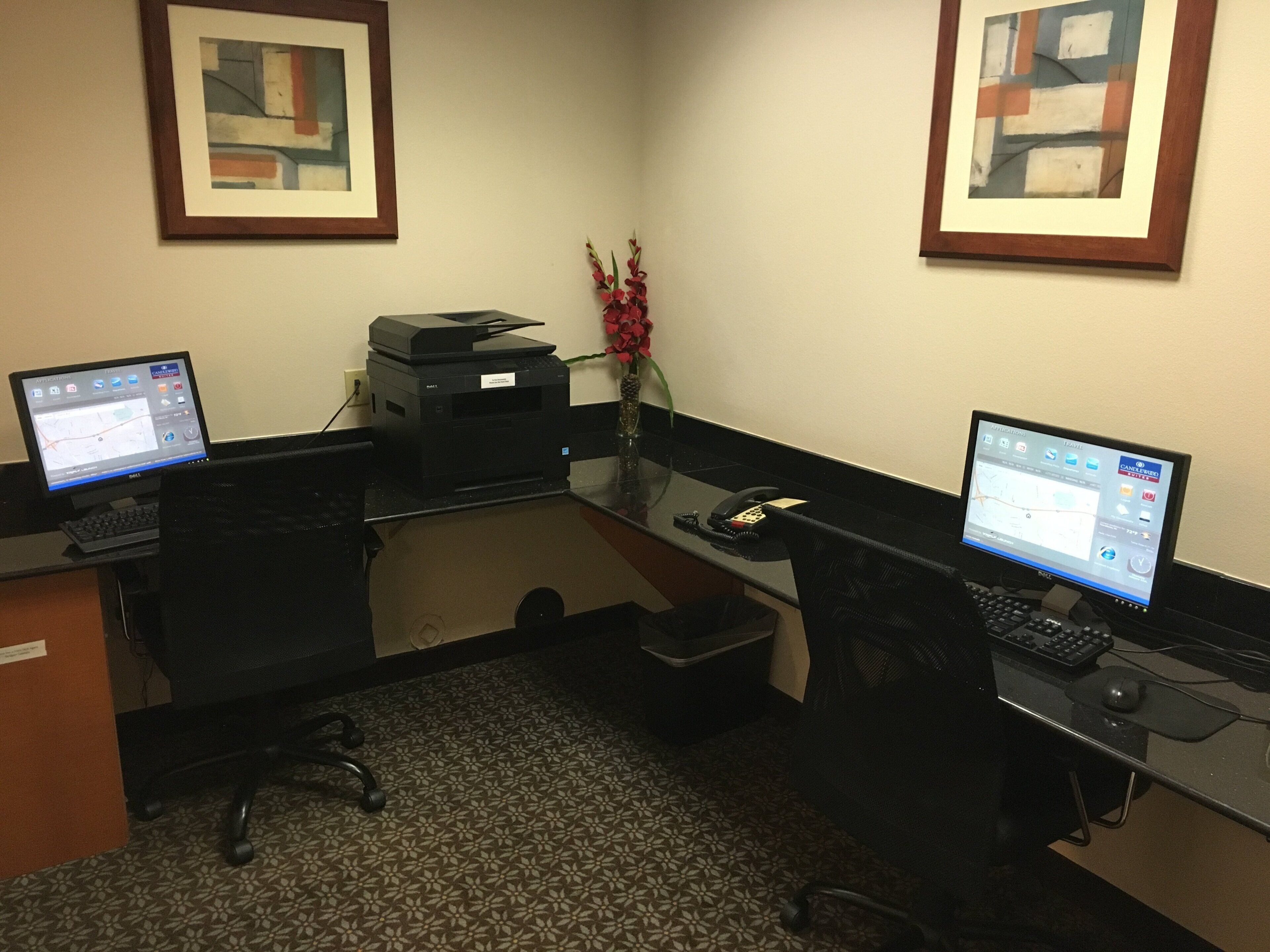 A workspace with two desks, computers, a printer, and framed artwork on the wall.