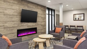 A modern lounge area with a flat-screen TV, a fireplace, comfortable seating, and a large mirror on the wall. - Candlewood Suites Tuscaloosa by IHG (Tuscaloosa)
