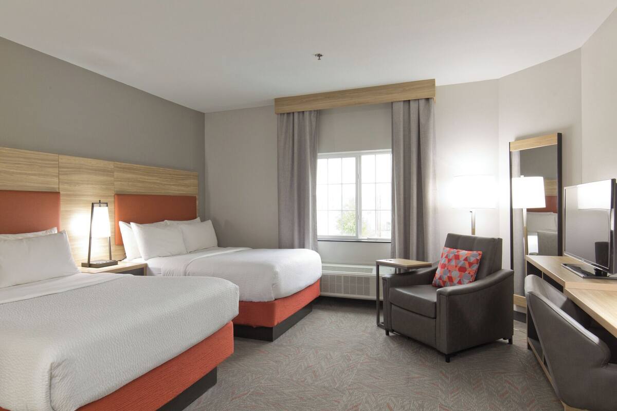 A hotel room with two beds, a desk, a chair, a TV, and a window with curtains.