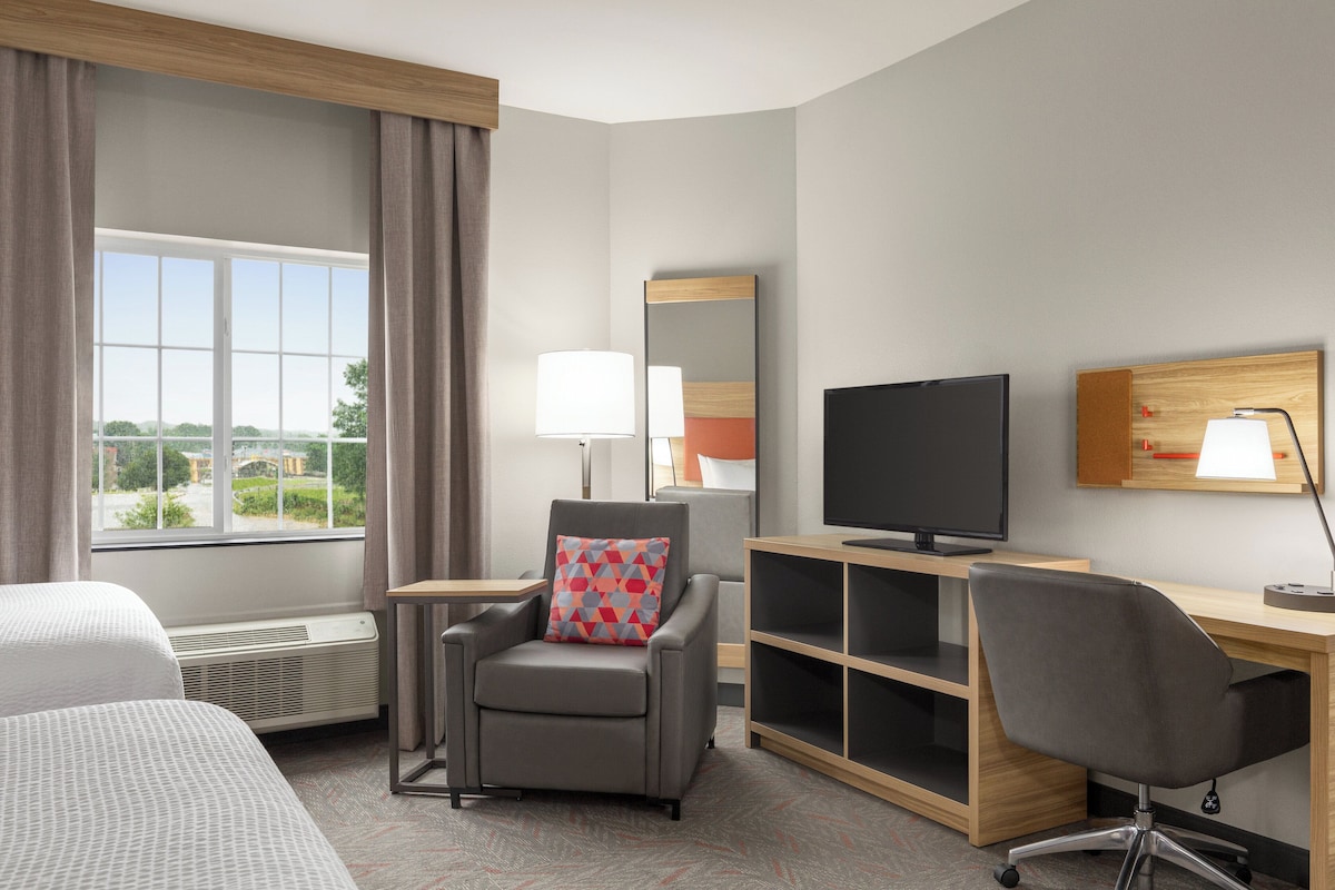 Une chambre d’hôtel avec une grande fenêtre, un bureau équipé d’un ordinateur, une télévision et une chaise.