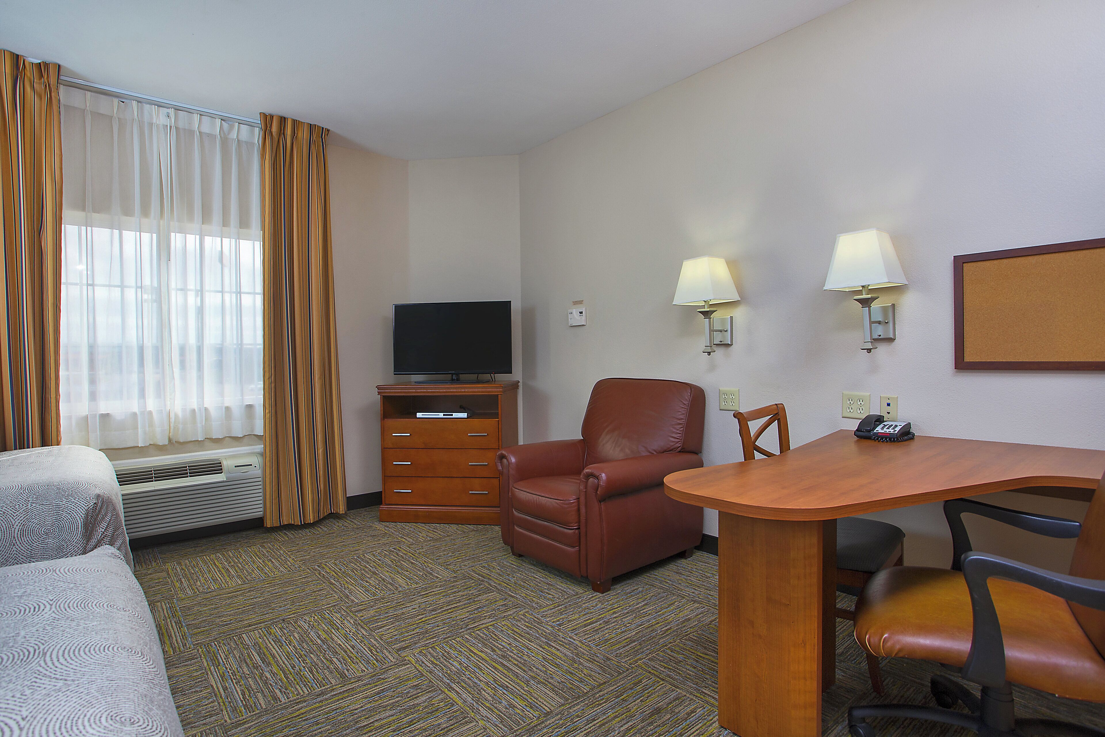 A hotel room with a bed, a desk with two chairs, a television, and a wall-mounted telephone.