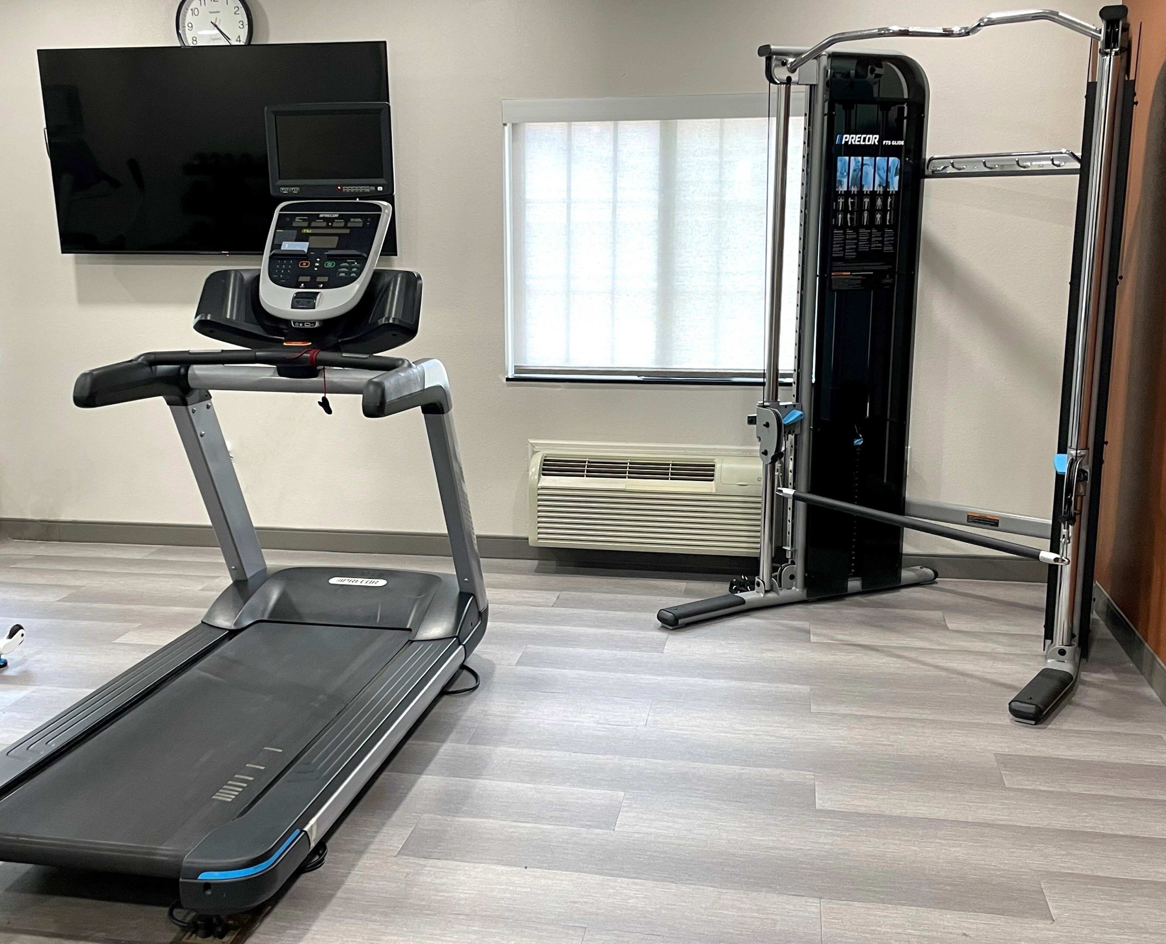 A gym with a treadmill, a weight machine, and a TV mounted on the wall.