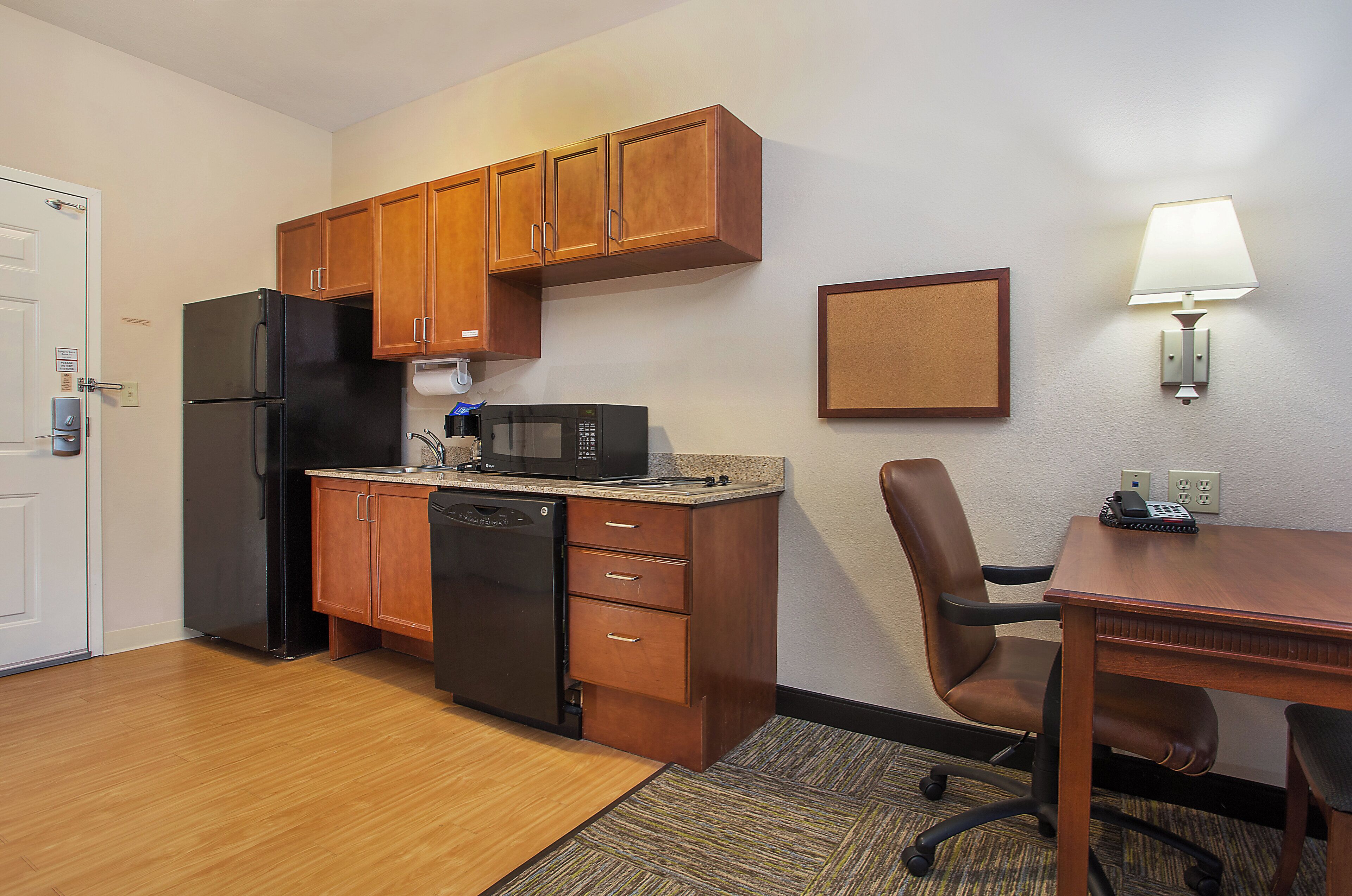 A compact kitchen with wooden cabinets, a black refrigerator, a microwave, and a small dining area with a table and chair.