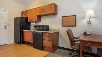 A compact kitchen with wooden cabinets, a black refrigerator, a microwave, and a small dining area with a table and chair.