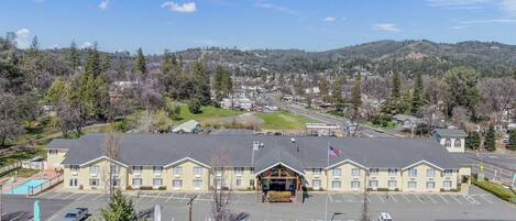 A large building with a parking lot in front, surrounded by trees and hills.