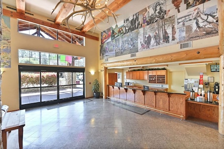 A spacious lobby with a reception desk, wooden paneling, a large mural, and a view through the glass doors.