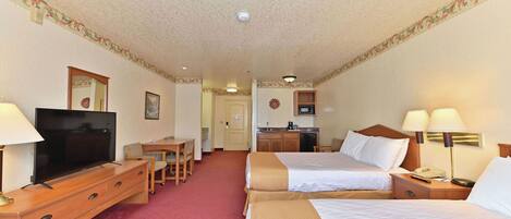 A hotel room with two beds, a TV, a desk, a kitchenette, and a red carpet.