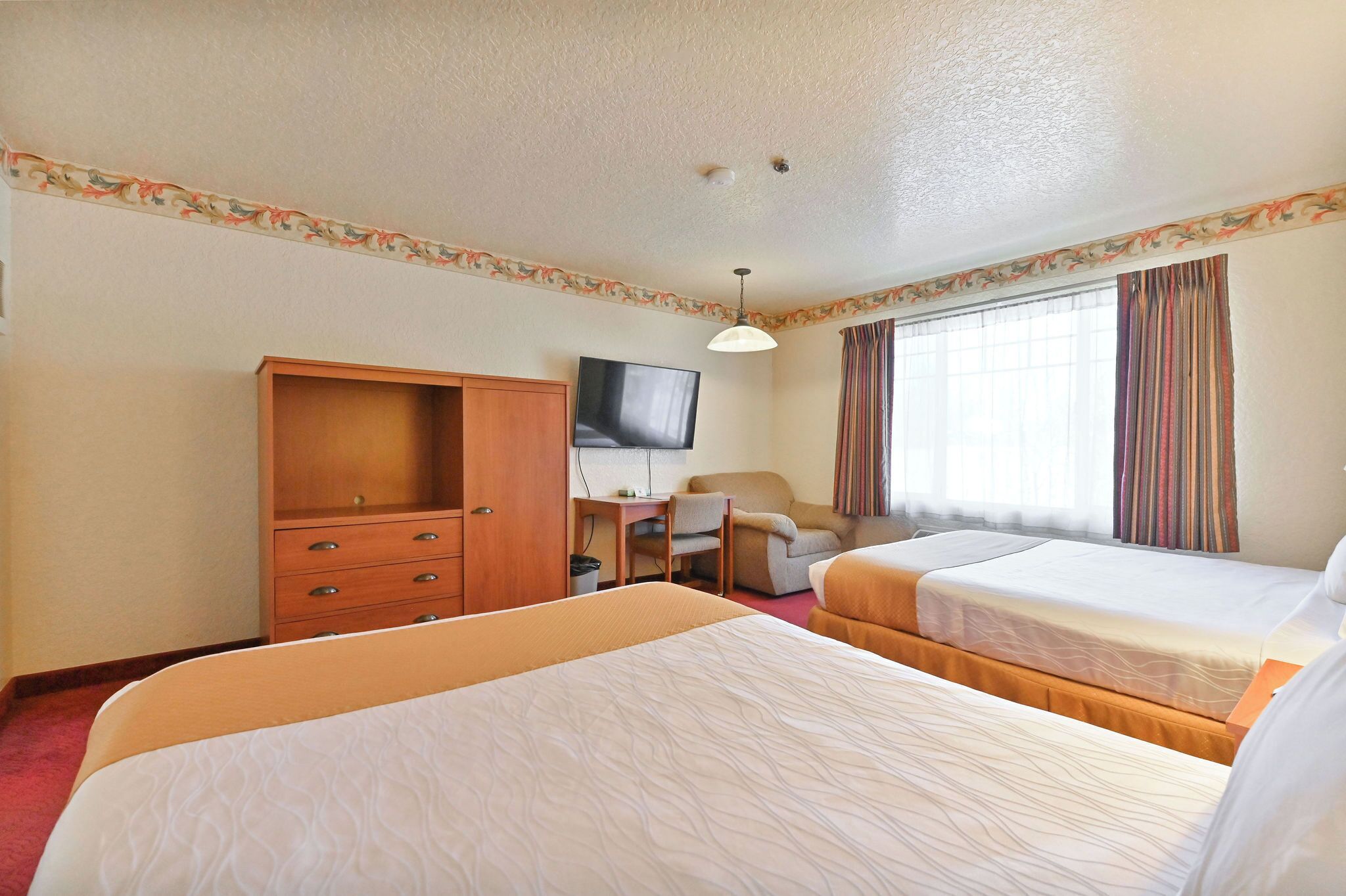 A hotel room with two beds, a desk, a television, and a wardrobe.