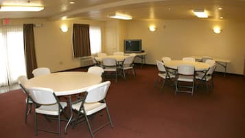 A conference room with multiple tables and chairs, a television, and an exit sign.