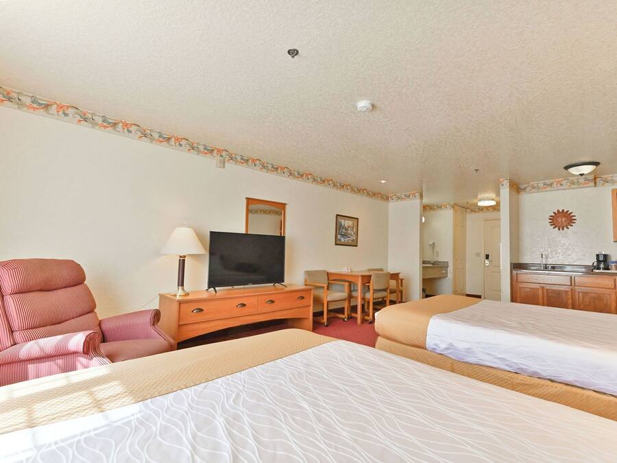 A hotel room with two beds, a TV, a desk, and a kitchenette.