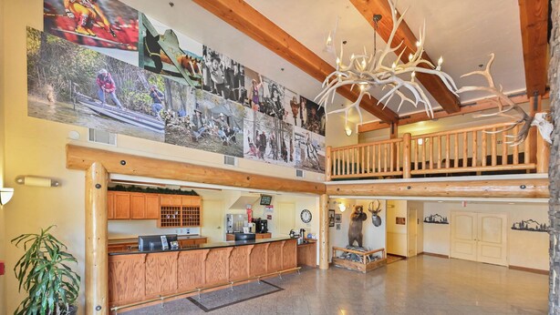 A hotel lobby with a wooden reception desk, a large photo collage on the wall, a chandelier, and a bear statue.