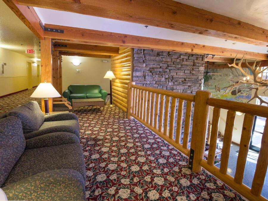Un hall de hotel con alfombra estampada, un sofá verde, barandilla de madera y pared de piedra con un mural.