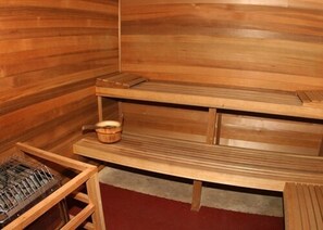 A wooden sauna with a bench, a shelf with a basket, and a sauna heater.