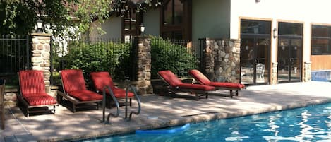 Zona junto a la piscina con sillones de descanso y una pared de piedra.