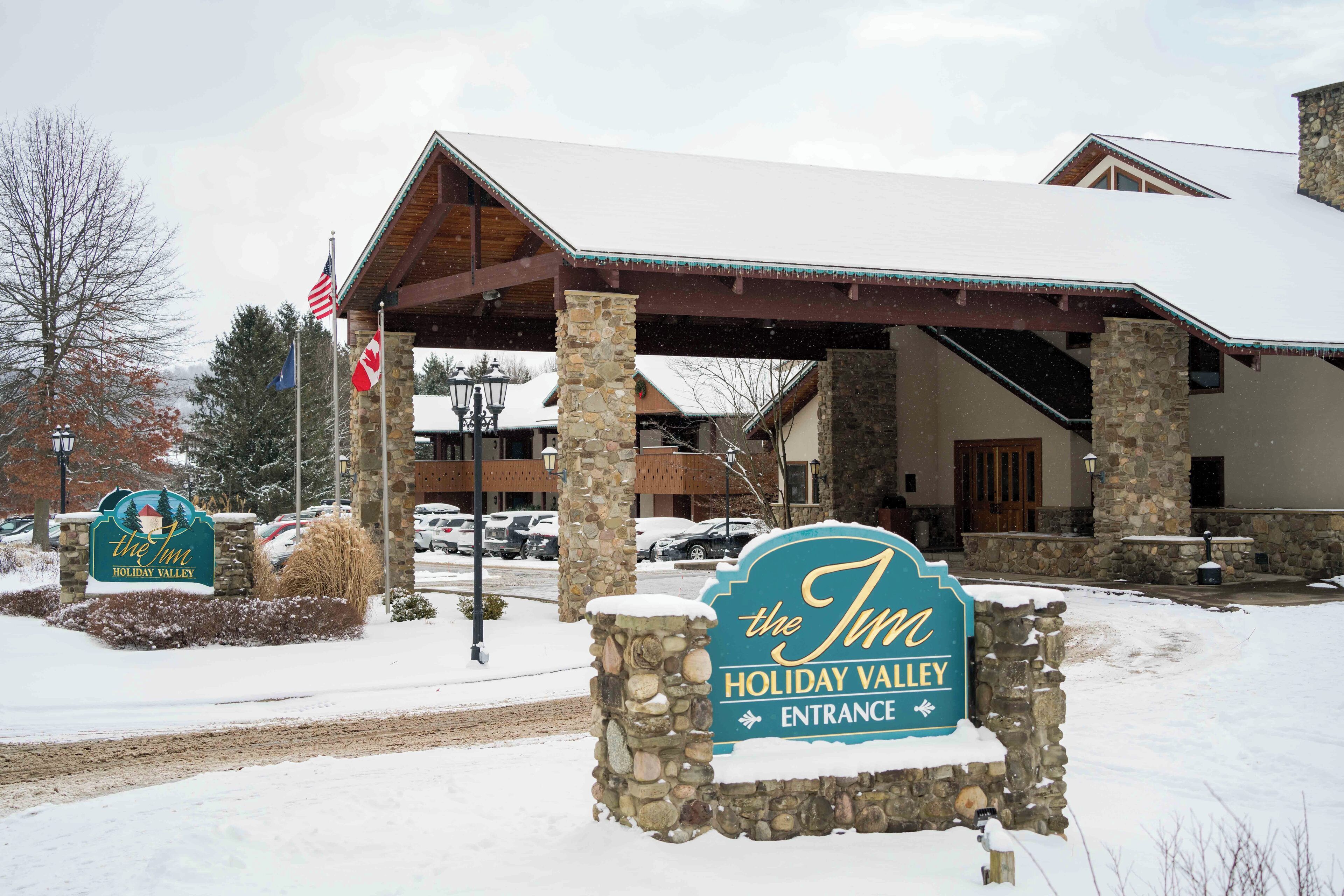 A hotel entrance with a stone sign, American flag, and a covered area with stone pillars.