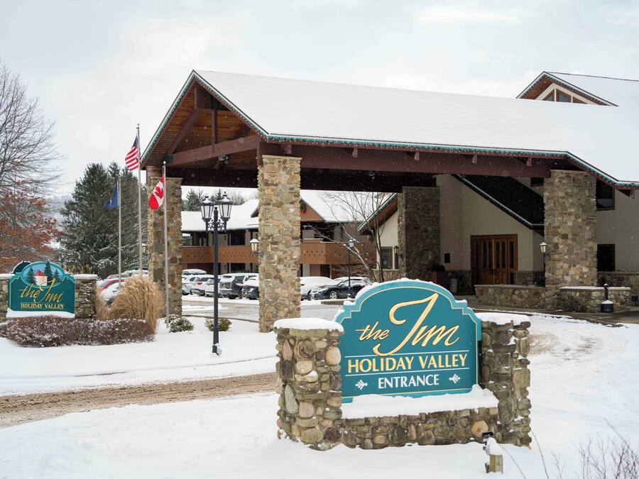 A hotel entrance with a stone sign, American flag, and a covered area with stone pillars.
